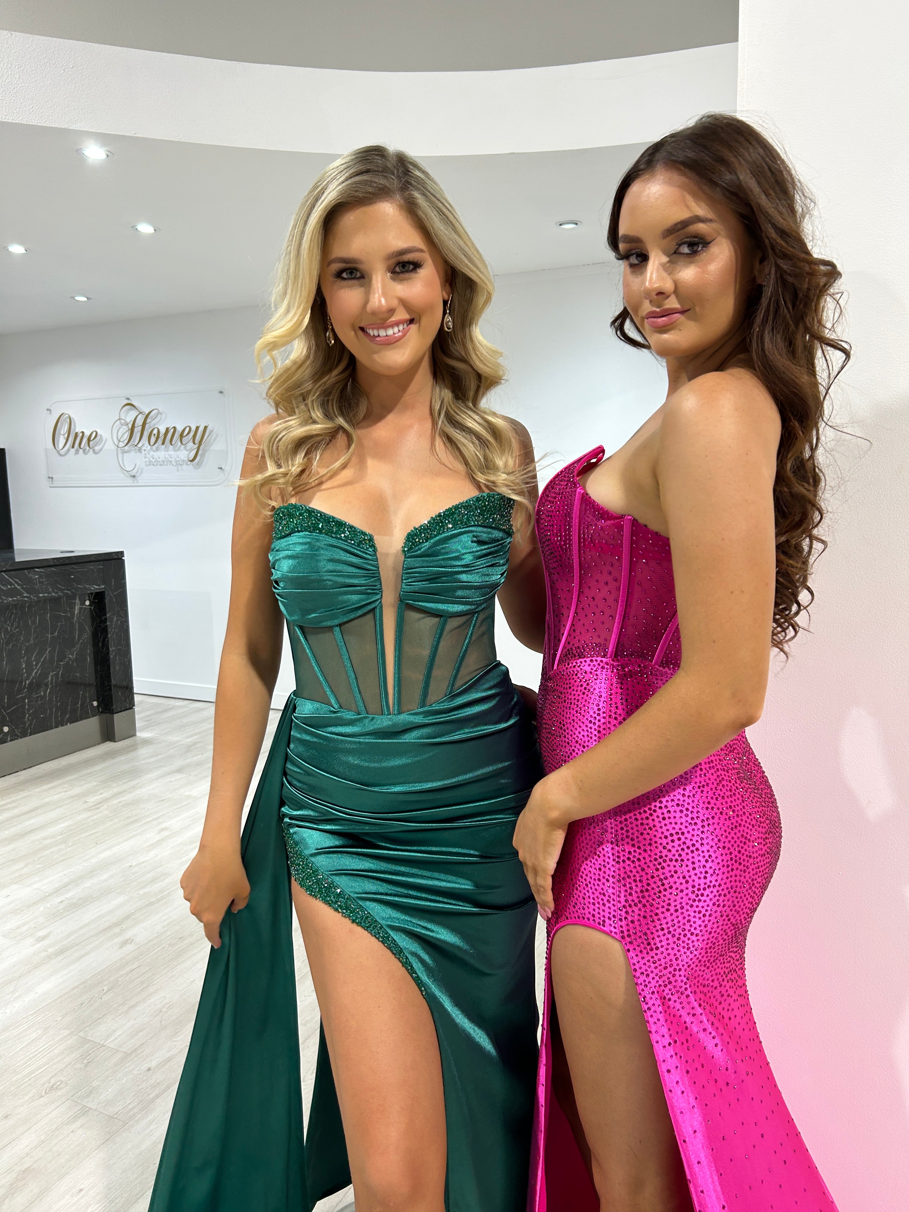 Two women in glamorous strapless evening gowns, one in emerald green with a sheer boned corset and the other in sparkly pink. Brisbane to Gold Coast