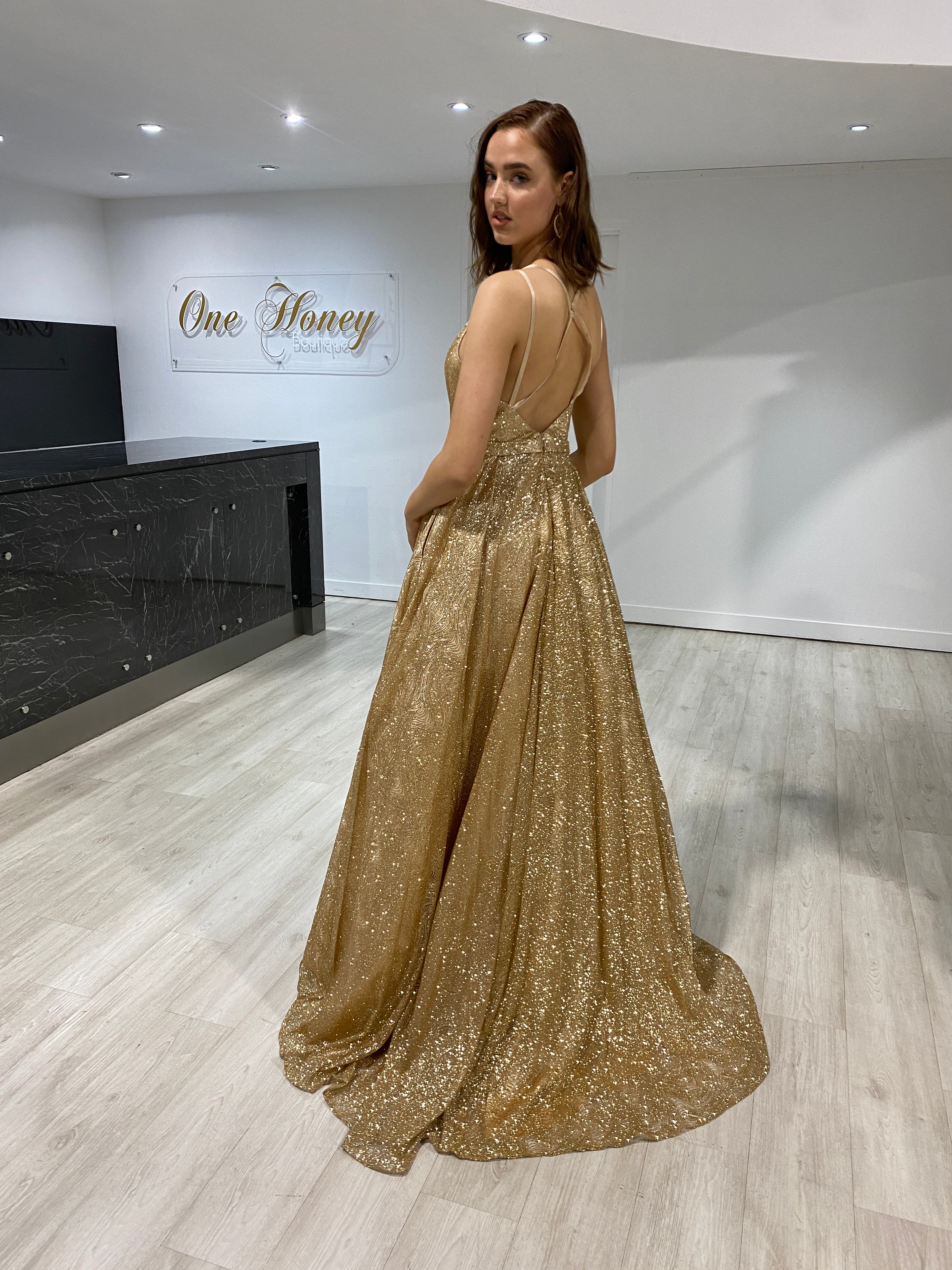 Model wearing Honey Couture GRETCHEN gold glitter ball gown, an elegant evening dress with tulle lining, perfect for formal occasions by an Australian designer.