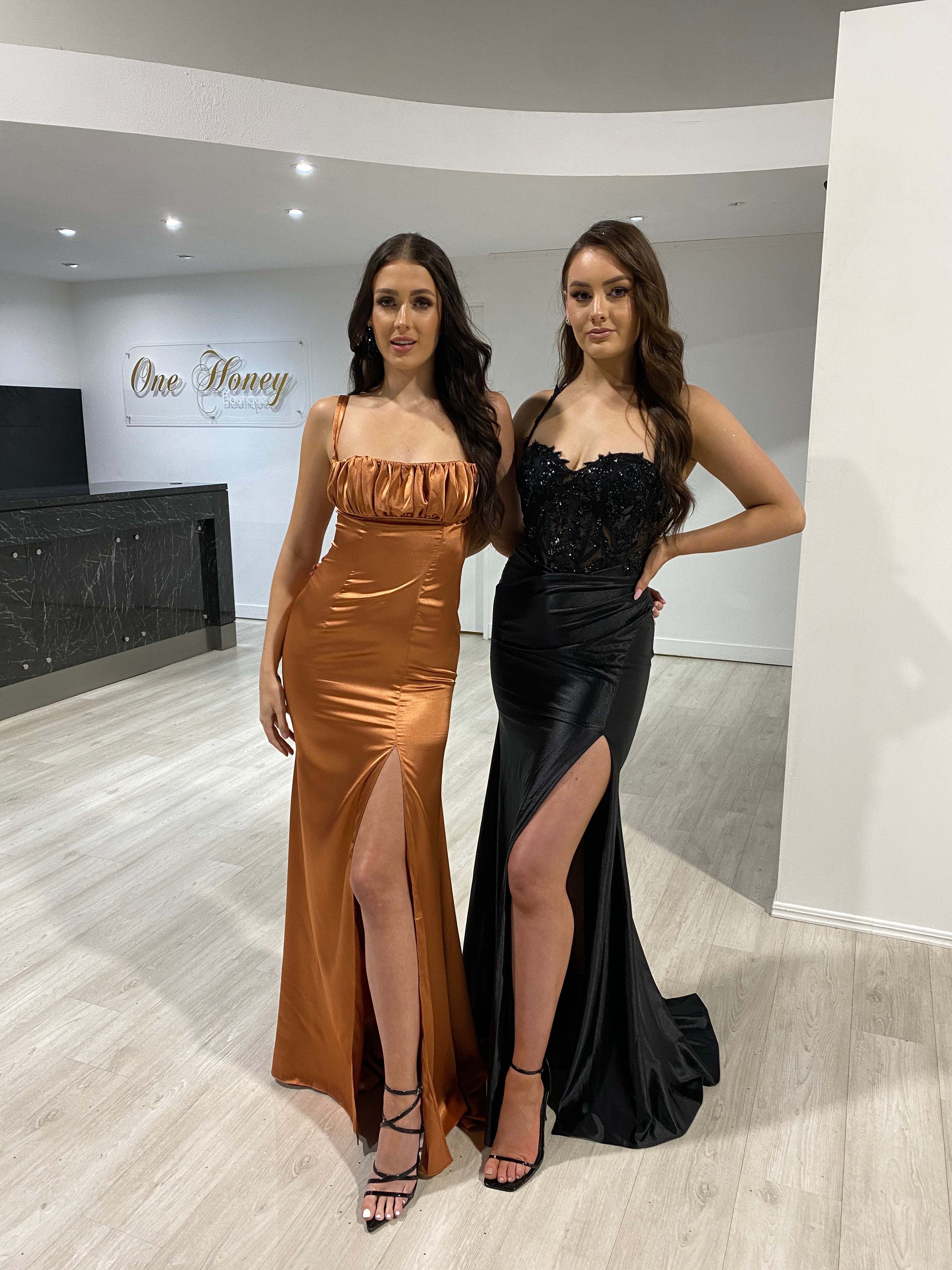 Satin slit evening gowns, burnt orange and black with ruched busts, in a showroom setting. Brisbane to Gold Coast, Australia.