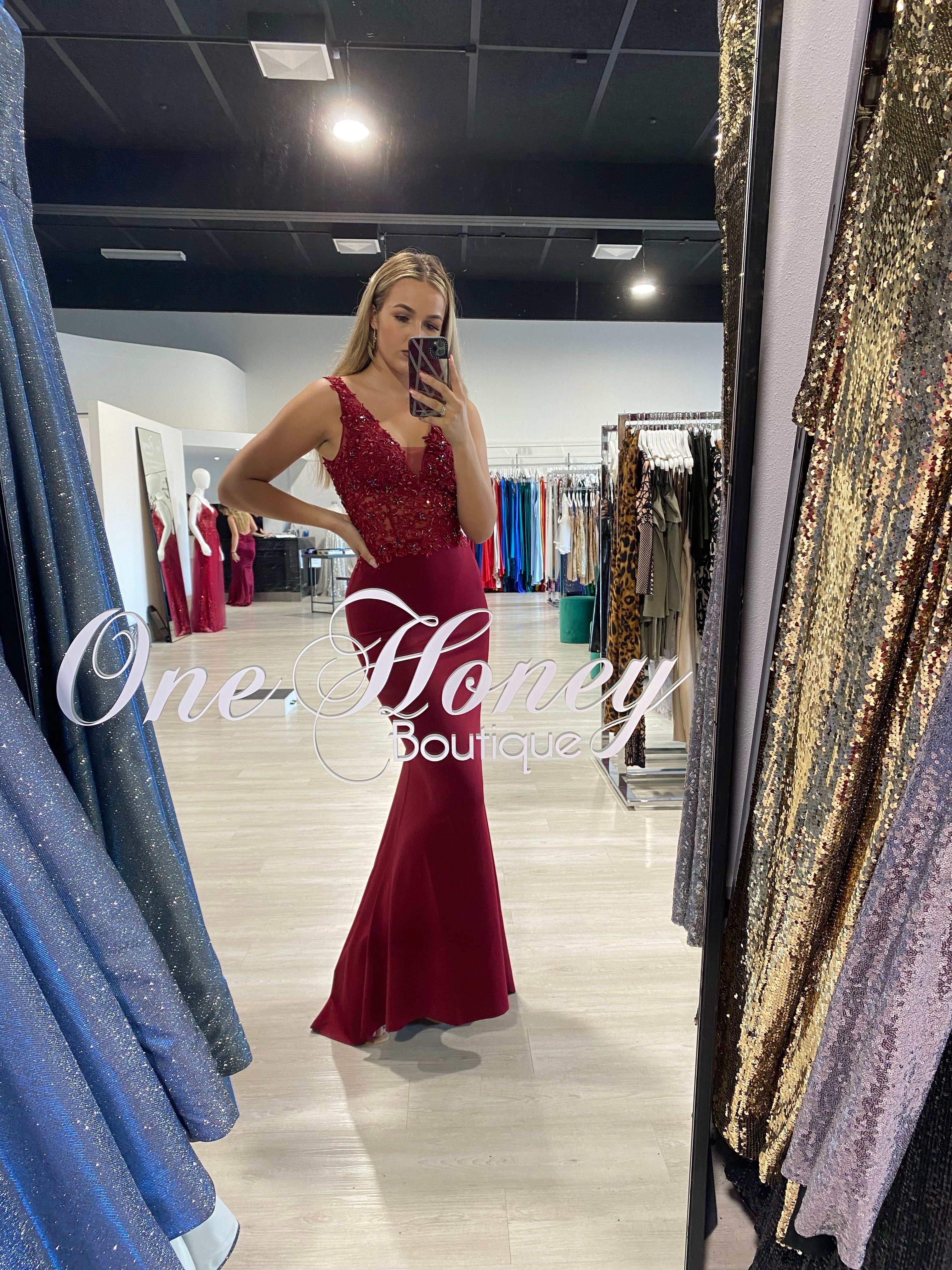 Woman in Honey Couture ISLA Burgundy beaded lace formal dress at boutique showroom.
