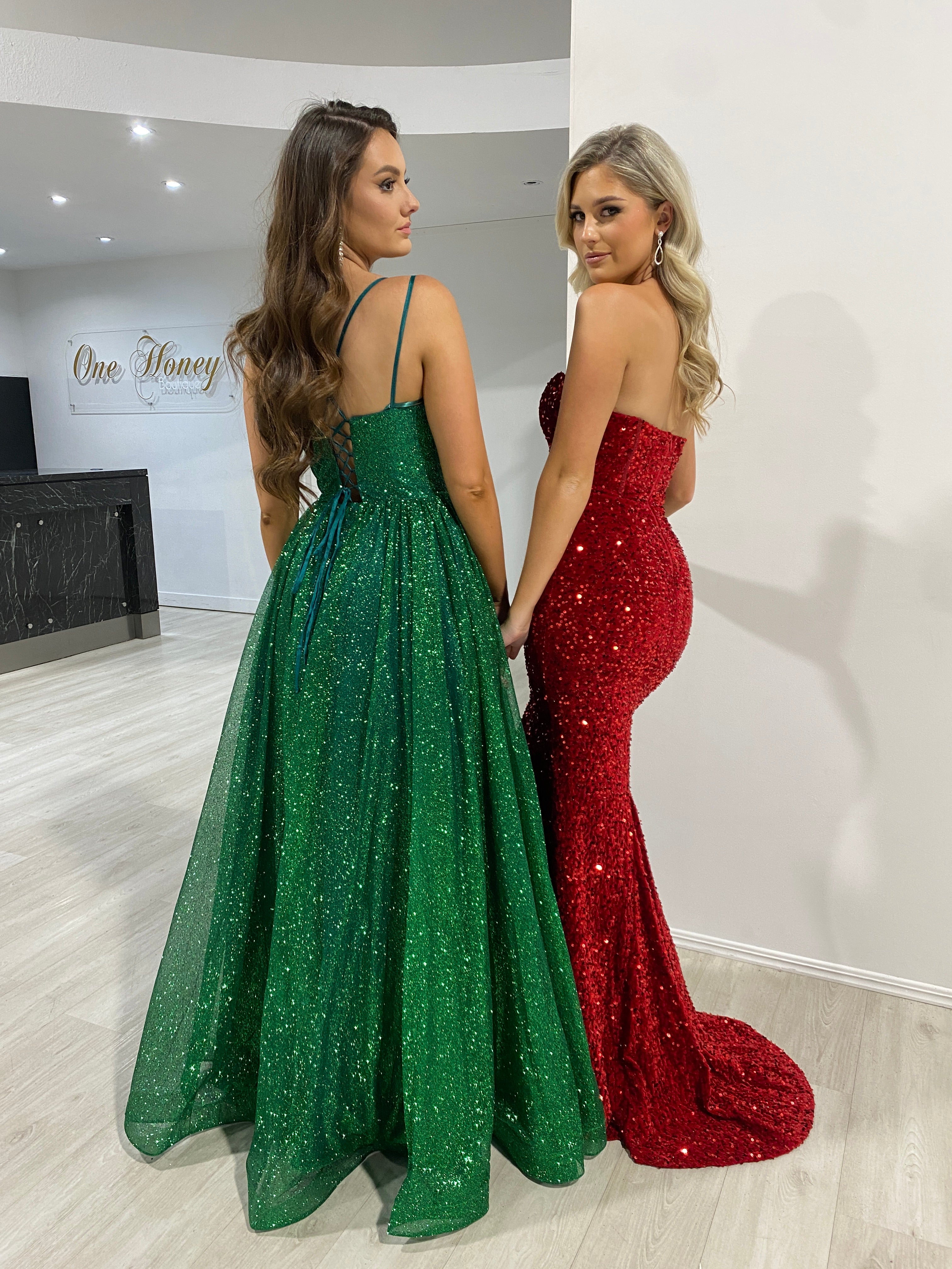 Two women in glittering formal gowns; one in a green lace-up ball gown, the other in a red strapless dress. Brisbane to Gold Coast, Australia.