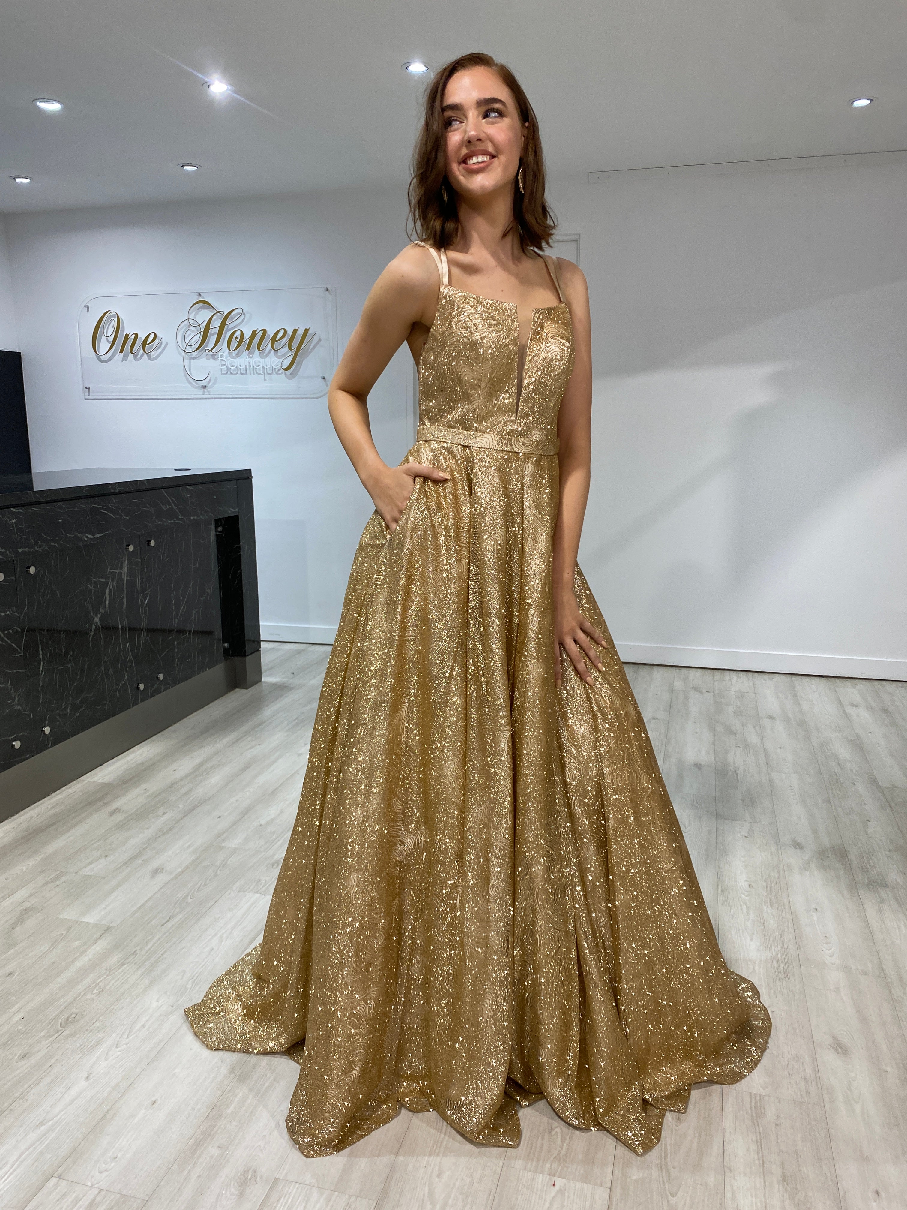 Woman wearing Honey Couture GRETCHEN gold glitter ball gown, designed by Australian designer, perfect for prom or special occasions.