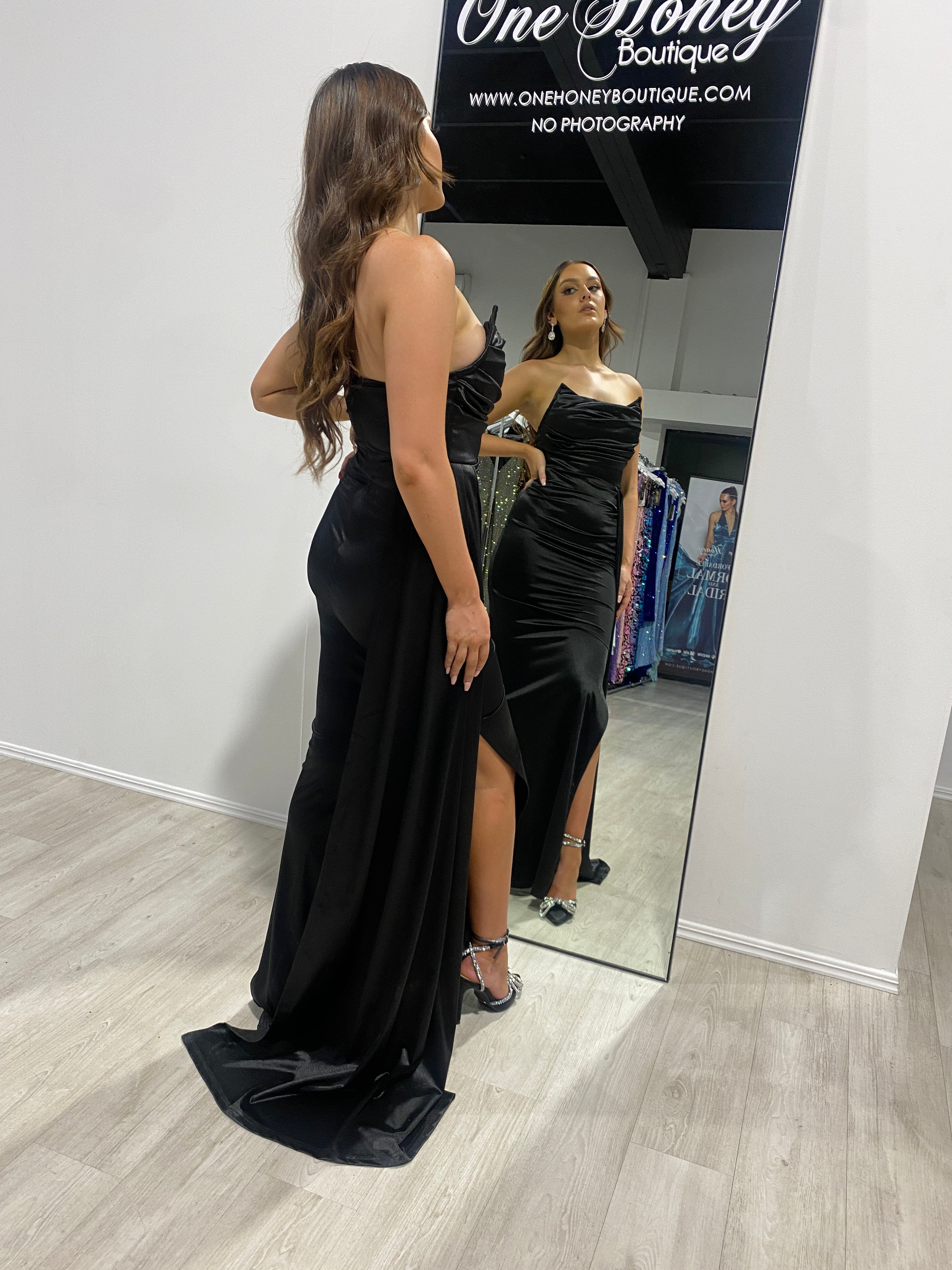 Woman wearing Honey Couture JAEDA black strapless mermaid gown, viewing herself in a mirror, showcasing evening elegance and Australian design.
