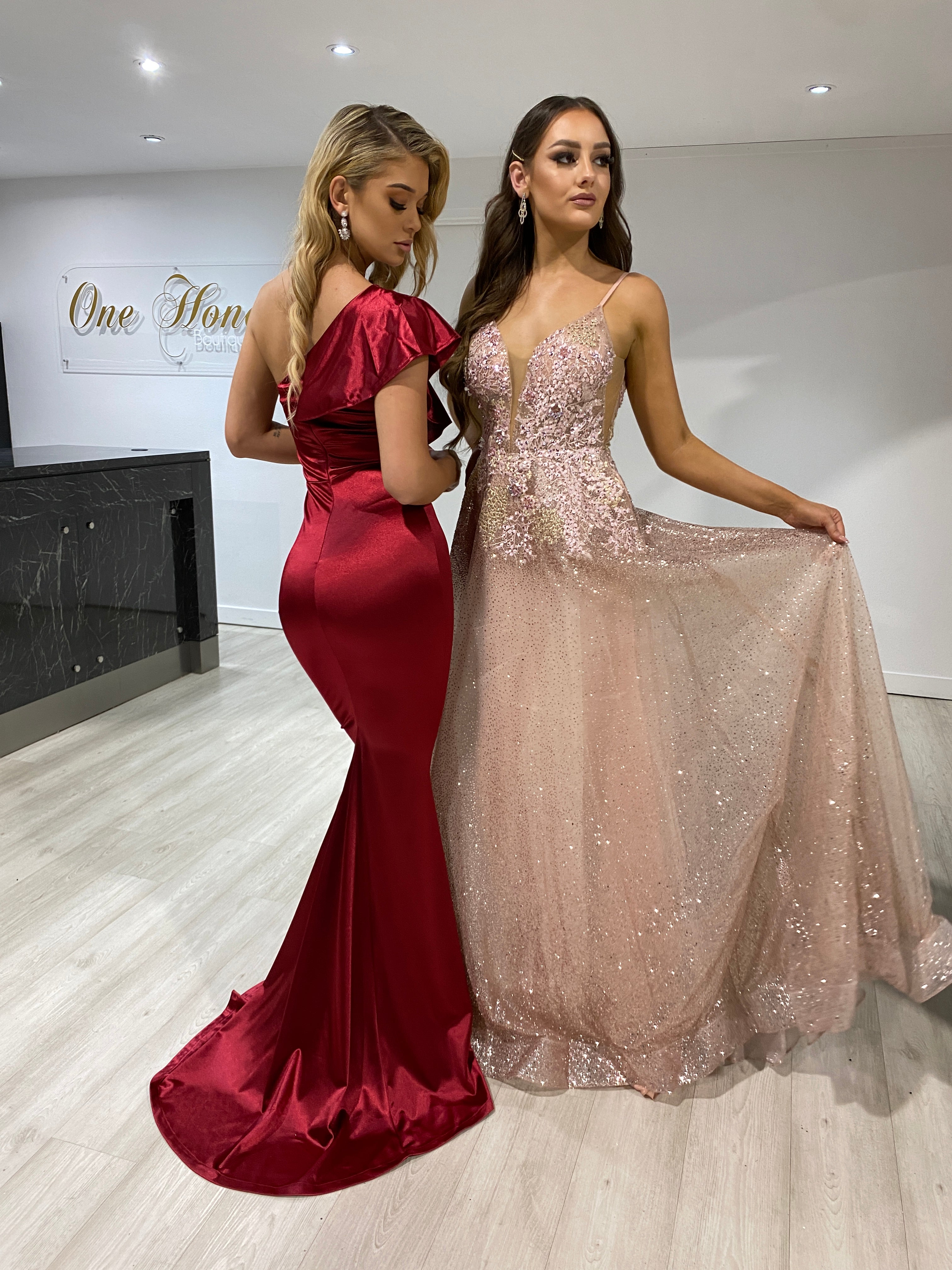 Two women wearing Honey Couture gowns: a red evening gown and the SIERRA rose gold & pink glitter ballgown. Australian designer prom dresses.