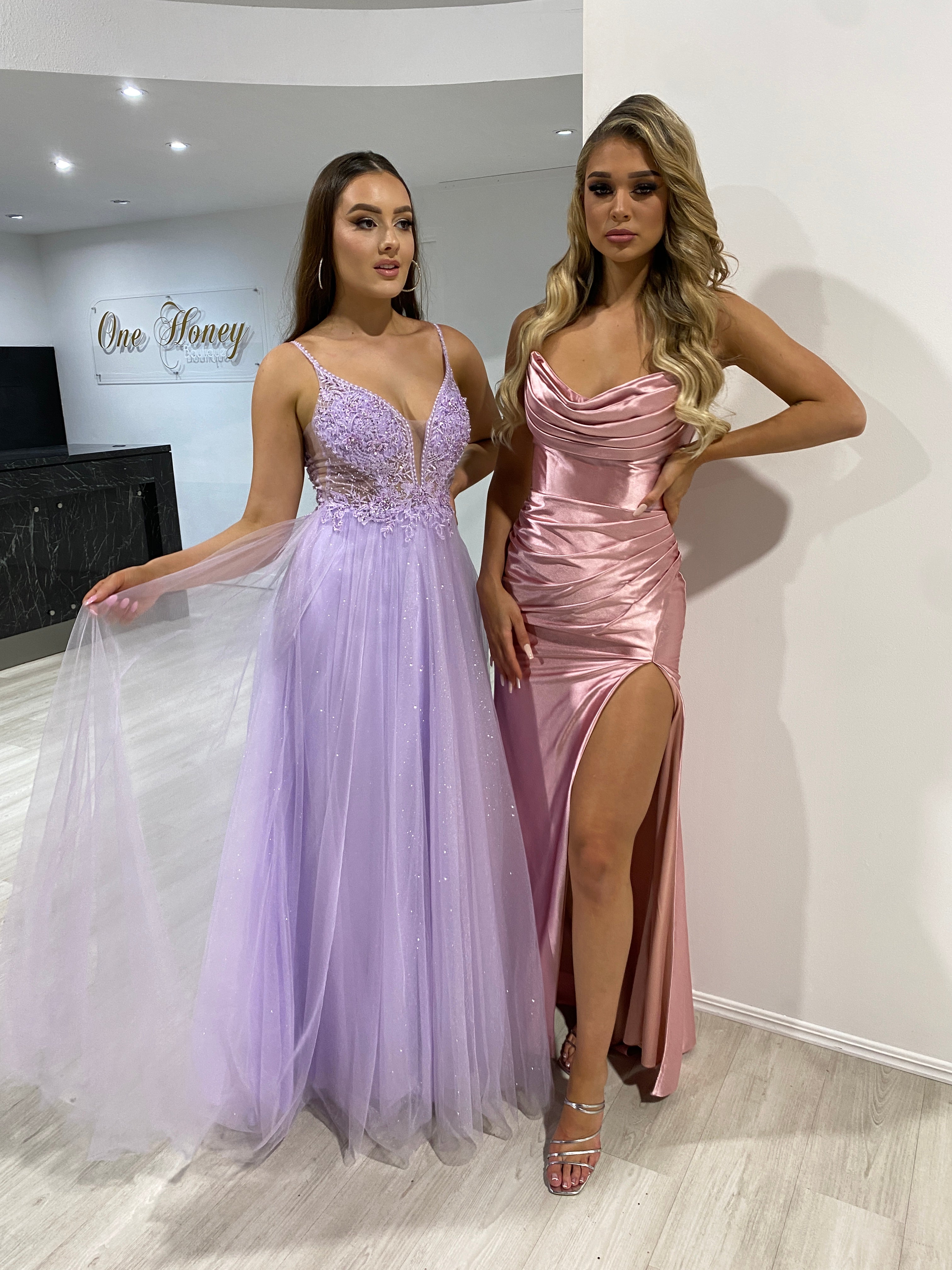 Two women in elegant evening gowns; one in a lavender tulle with beaded bodice, the other in a pink satin with a high slit. Brisbane to Gold Coast.