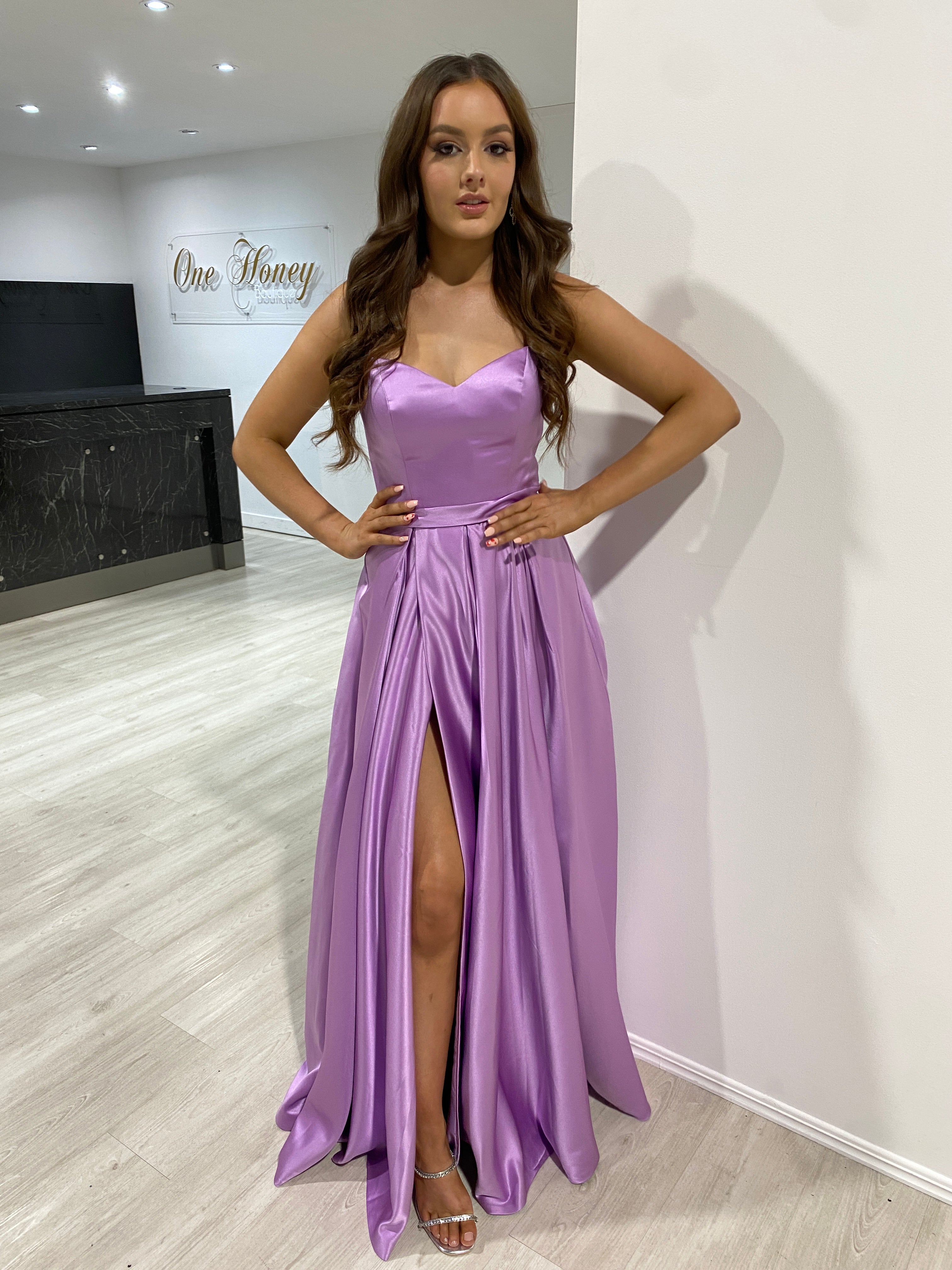 Woman wearing Honey Couture DANIELLA formal dress, featuring a corset lace-up back and box pleats. Perfect prom or evening gown.
