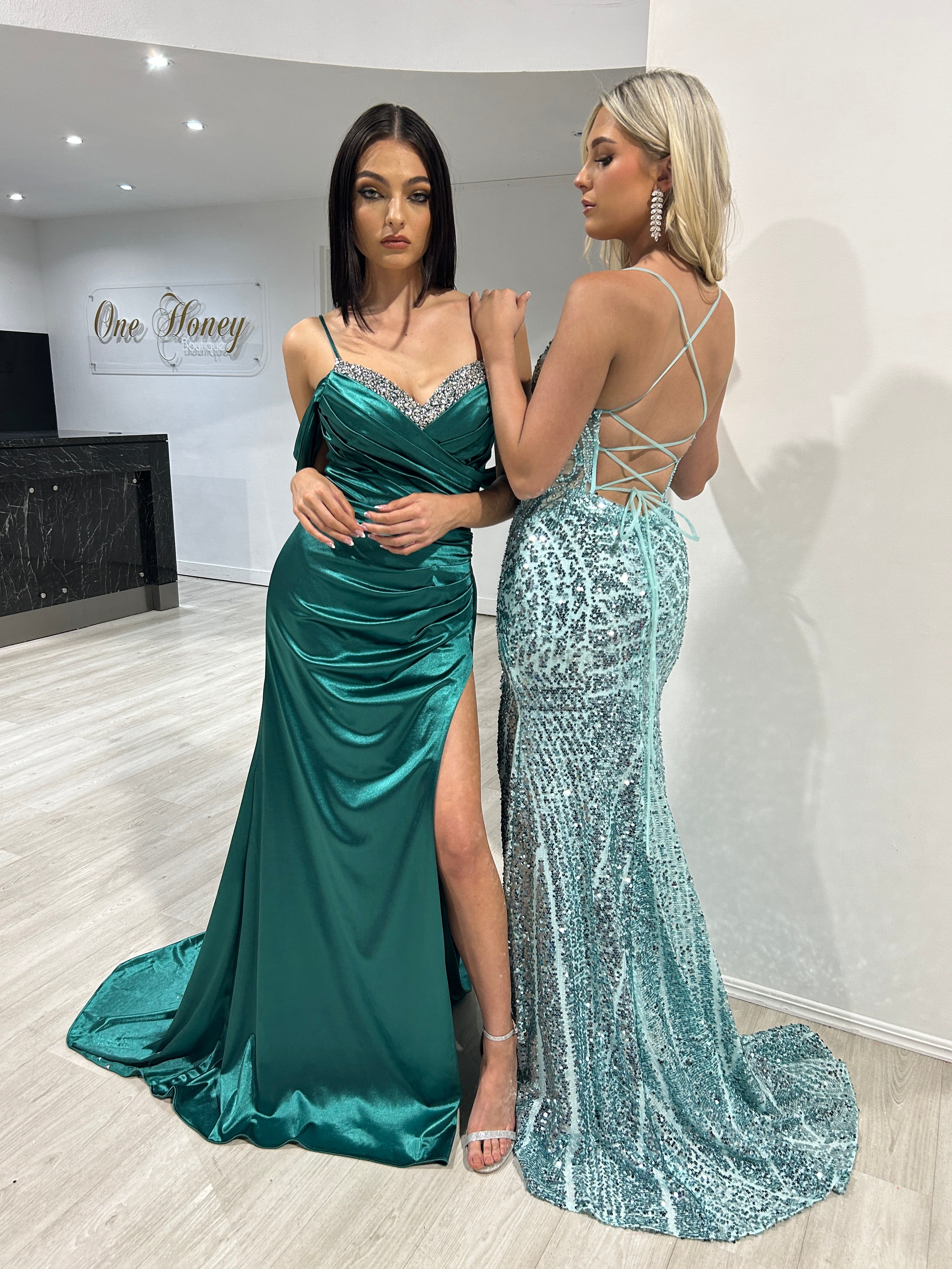 Two women in elegant evening gowns; one in emerald green satin with a thigh slit, the other in a sequined icy-blue dress. Brisbane to Gold Coast.