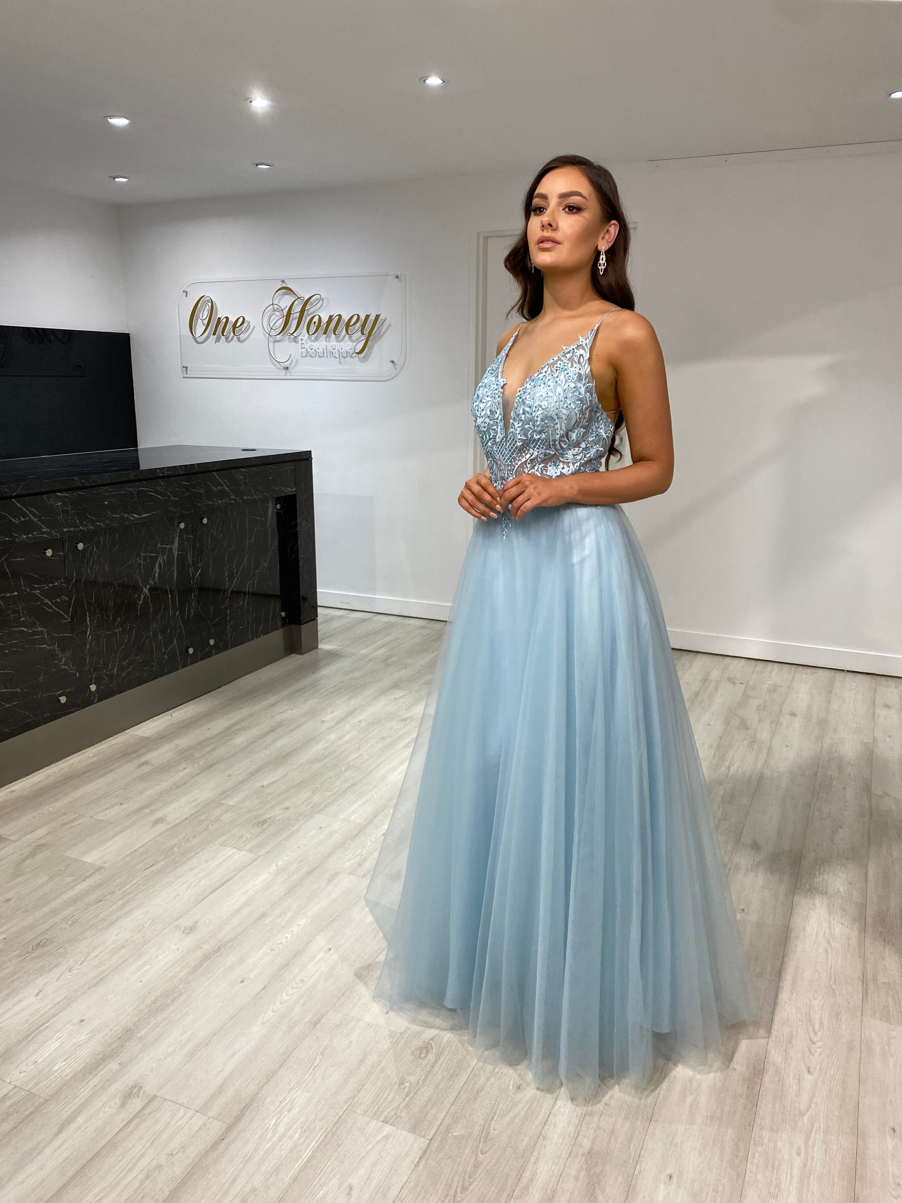Woman wearing Honey Couture INEZ Baby Blue Tulle Lace Gown with a full skirt and open back, perfect for prom or evening events.