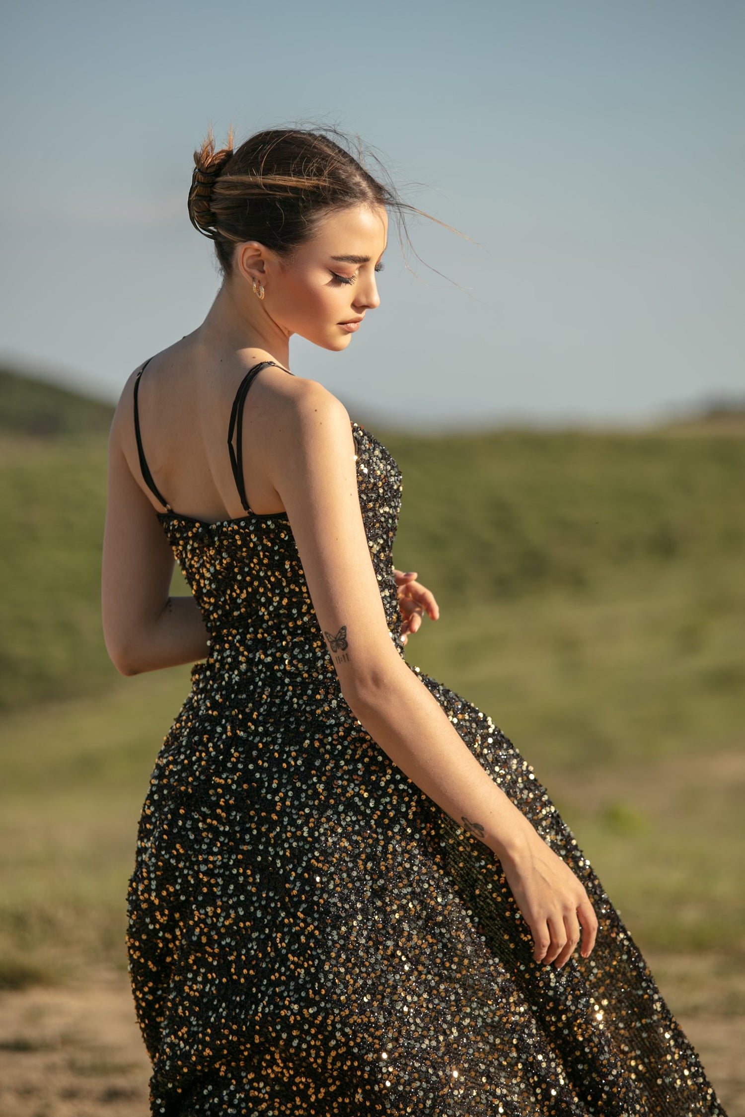 Woman in sequined black prom gown in a grassy field, showcasing elegant design. Scenic countryside backdrop. Brisbane to Gold Coast.